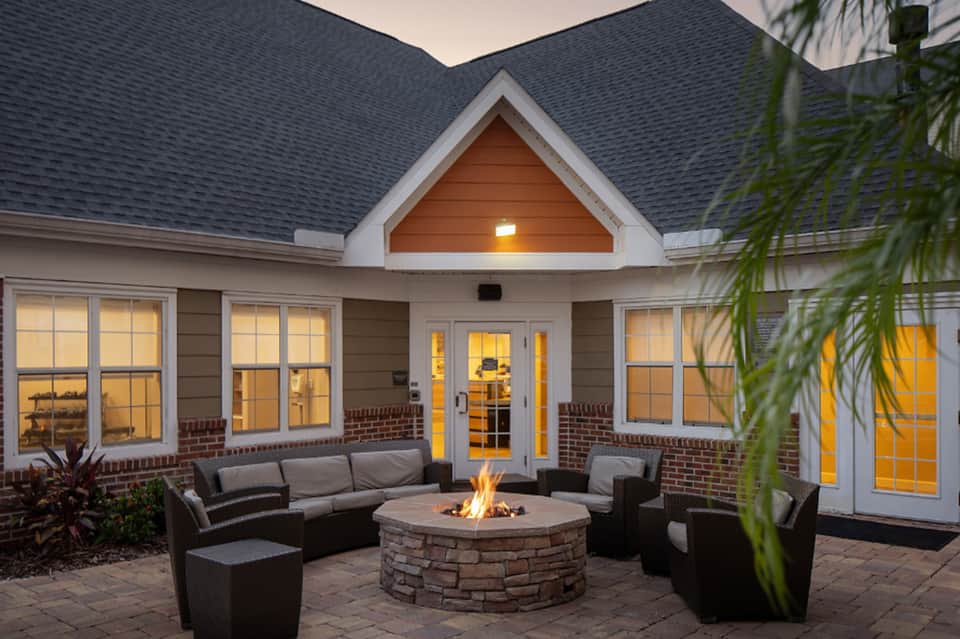 Modern house exterior at dusk with stone firepit, curved seating, and illuminated windows