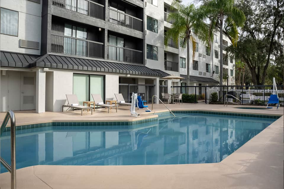 Resort pool deck with modern apartment building, lounge chairs, and palm trees