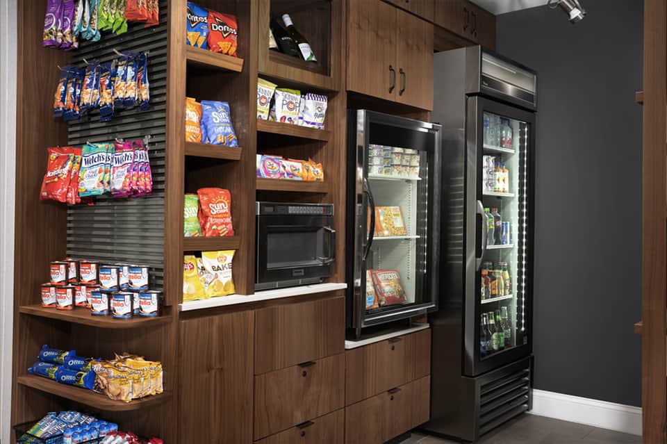 Snack station with wood shelving displaying colorful packaged items and refrigerated beverages