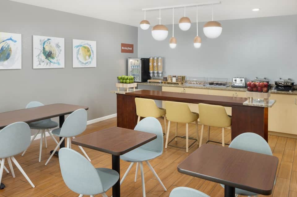 Bright break room with dining tables, yellow chairs, beverage station, and colorful wall art