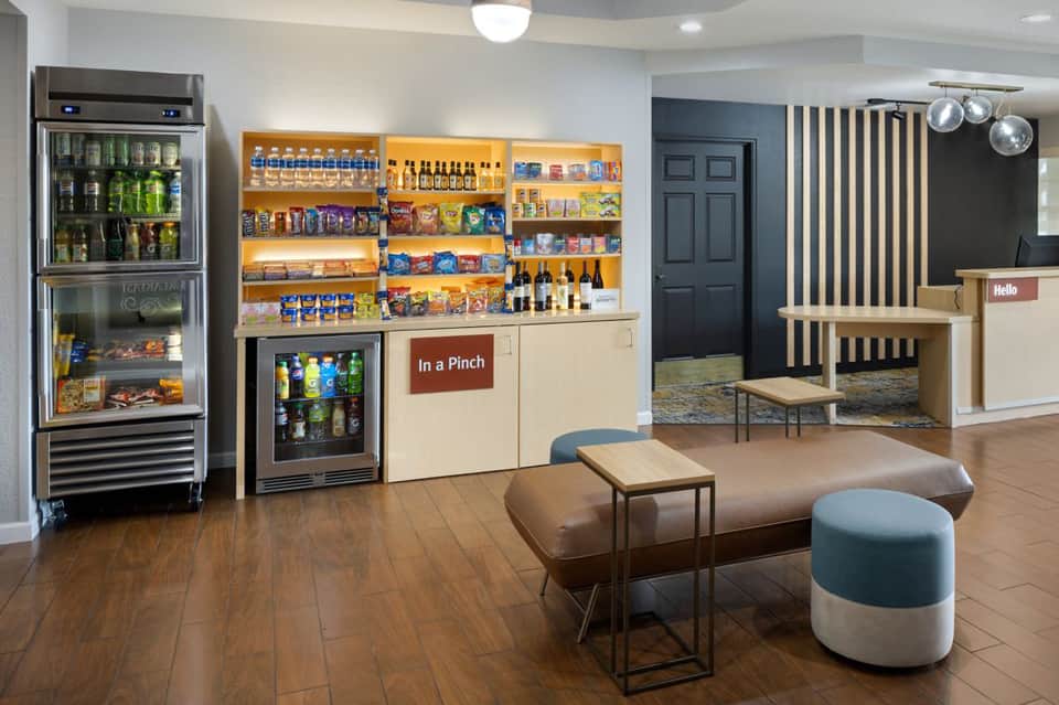 Hotel lobby and convenience store with beverage coolers, snacks, seating area, and check-in desk