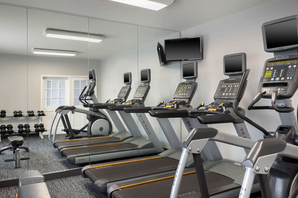 Fitness center with treadmills, exercise bikes, and wall-mounted monitors