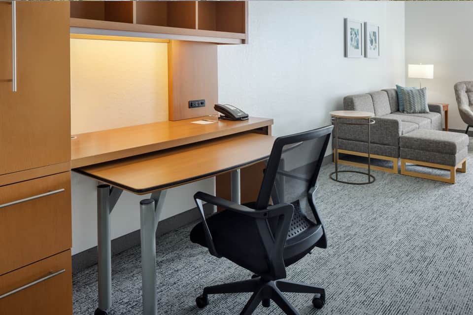 Hotel room workspace with desk, computer chair, and lounge seating area with natural light