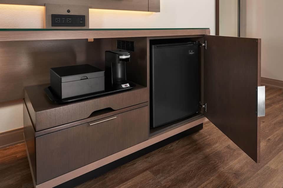 Hotel room mini bar with coffee maker, small refrigerator, and beverage station