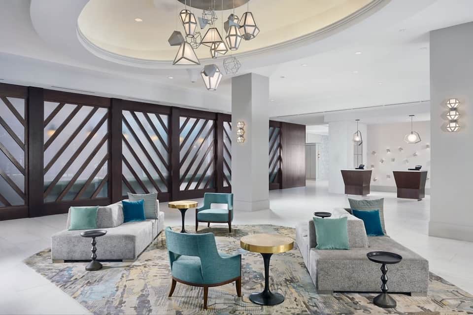 Modern hotel lobby with geometric pendant lighting, gray seating, teal accents, and geometric screens