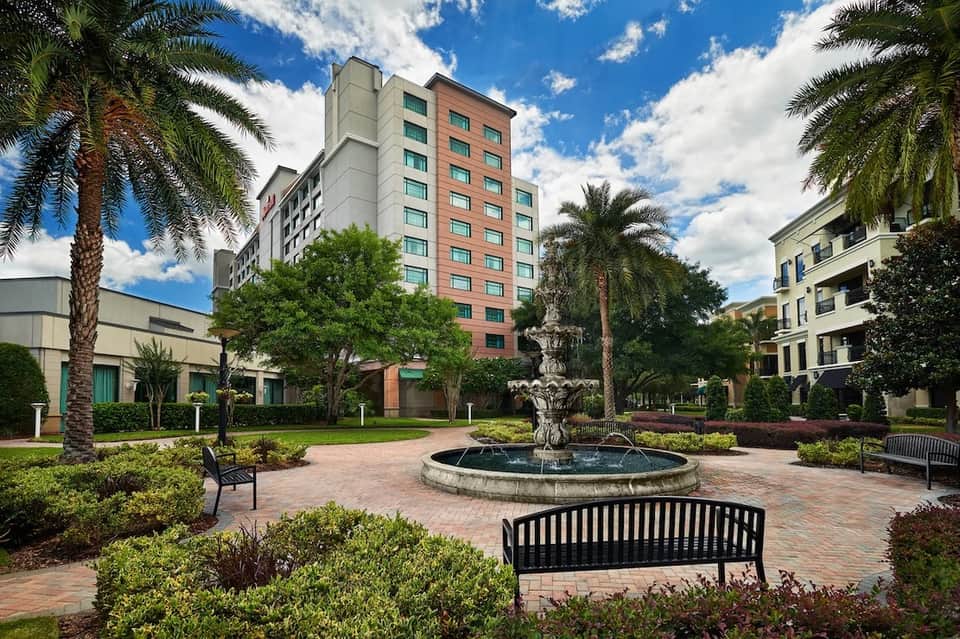 Resort courtyard with fountain, palm trees, manicured landscaping, brick pathways, and multi-story hotel building