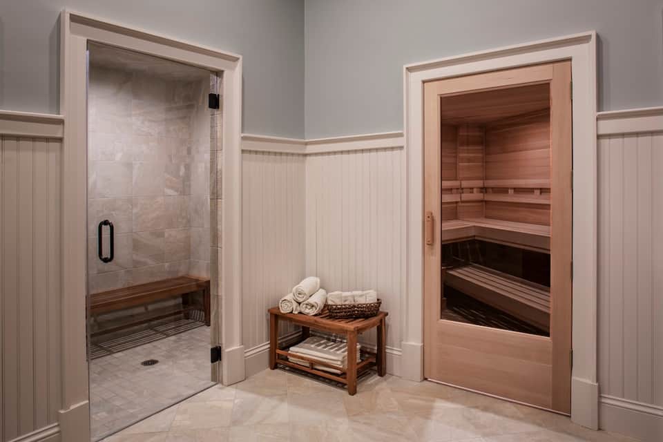 Spa area with steam shower, wooden sauna, white tile floors, and rolled towels on wooden bench