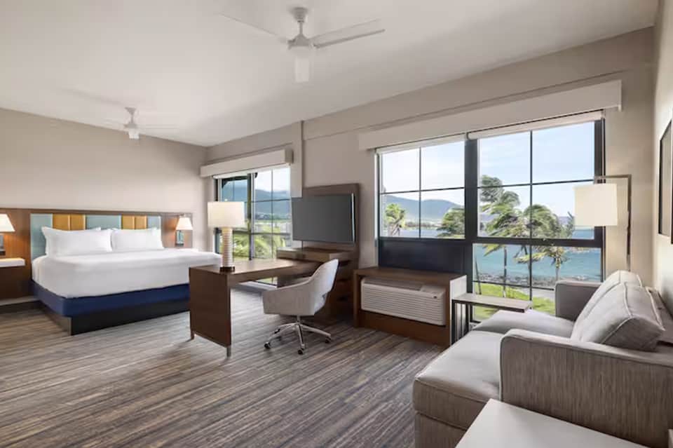 Hotel room with king bed, ocean view windows, work desk, and seating area