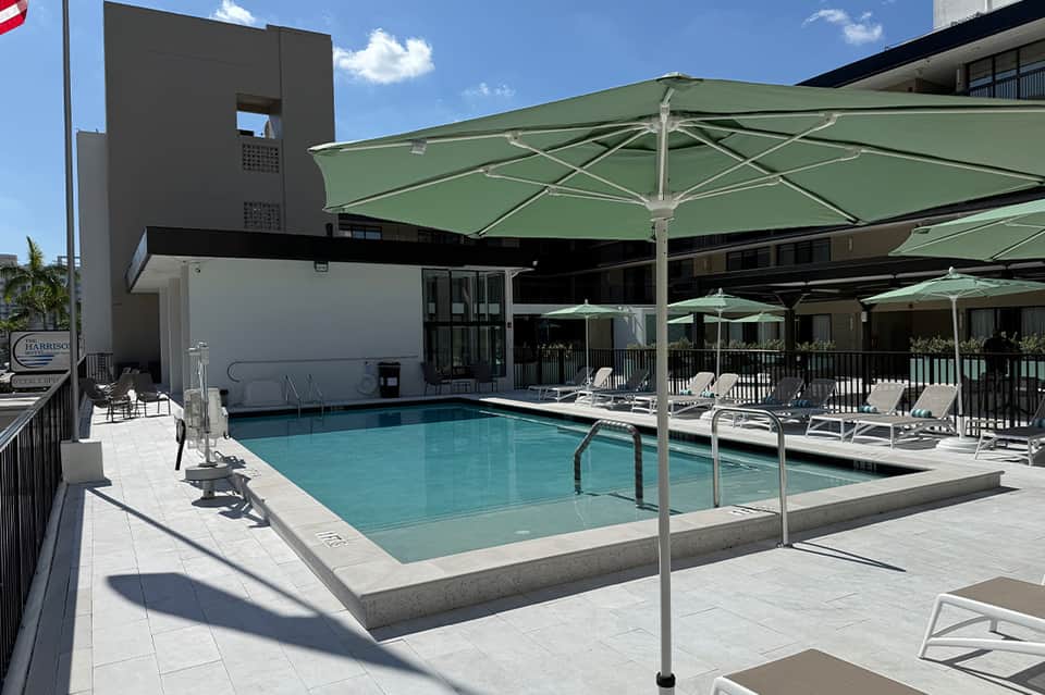 Resort pool with turquoise water under large green umbrellas, modern architecture and white loungers