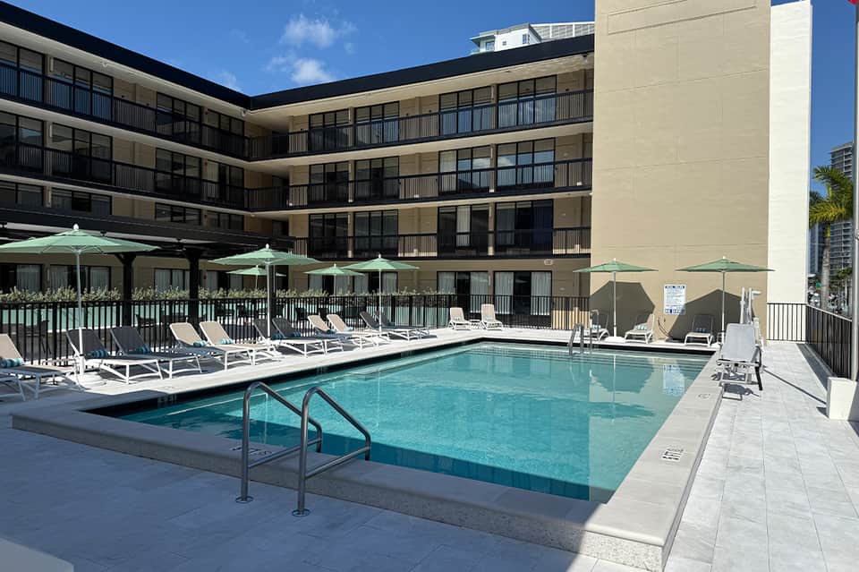 Outdoor pool surrounded by hotel courtyard with loungers and green umbrellas