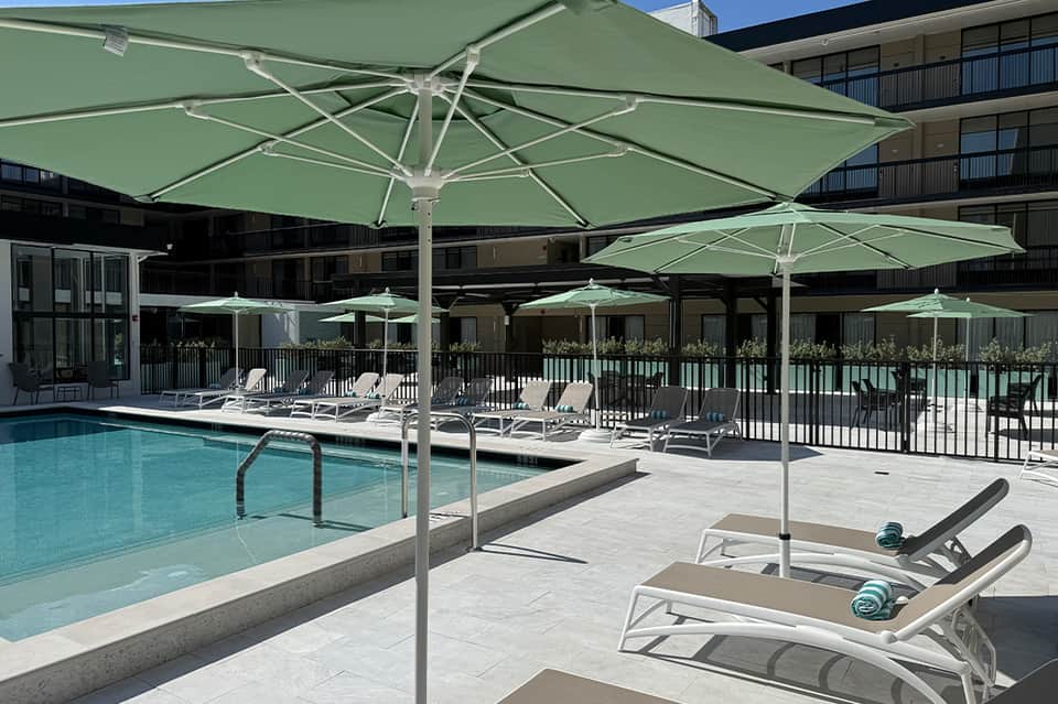Resort pool area with green umbrellas, lounge chairs, and hotel building