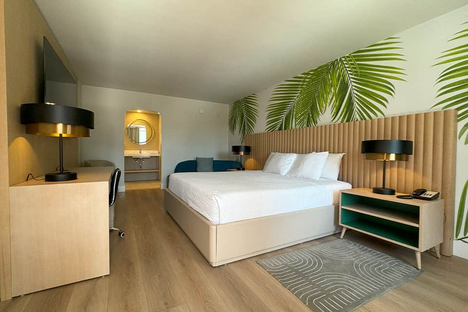 Contemporary hotel bedroom with palm leaf wallpaper, wooden headboard, and green accent furniture
