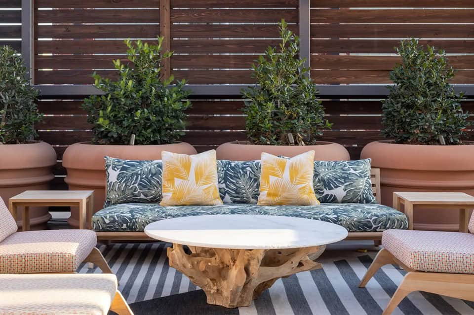 Outdoor lounge seating with wood sofa, patterned cushions, tropical plants, and coffee table