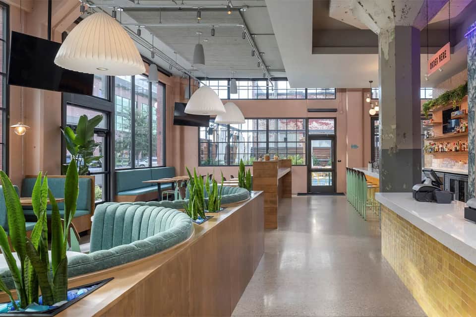 Contemporary cafe interior with teal seating, pendant lights, plants, large windows, and modern design elements