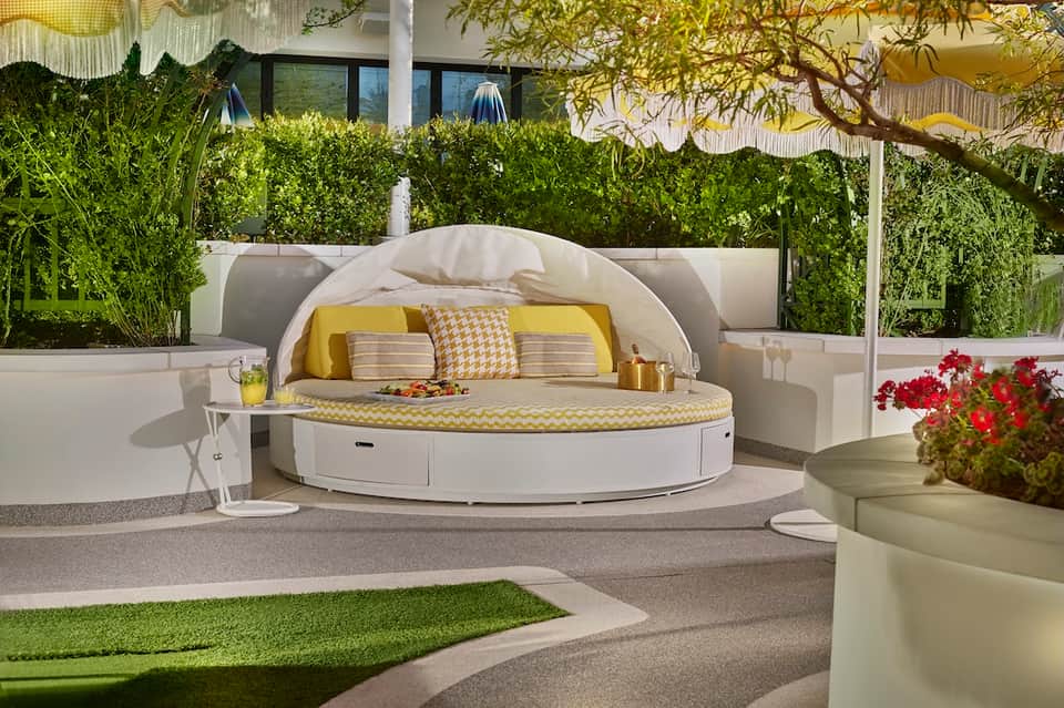 Luxurious round white daybed with yellow cushions on resort terrace with greenery