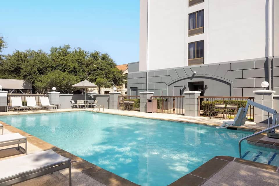 Modern hotel pool with clean blue water, loungers, architecture, and manicured landscaping