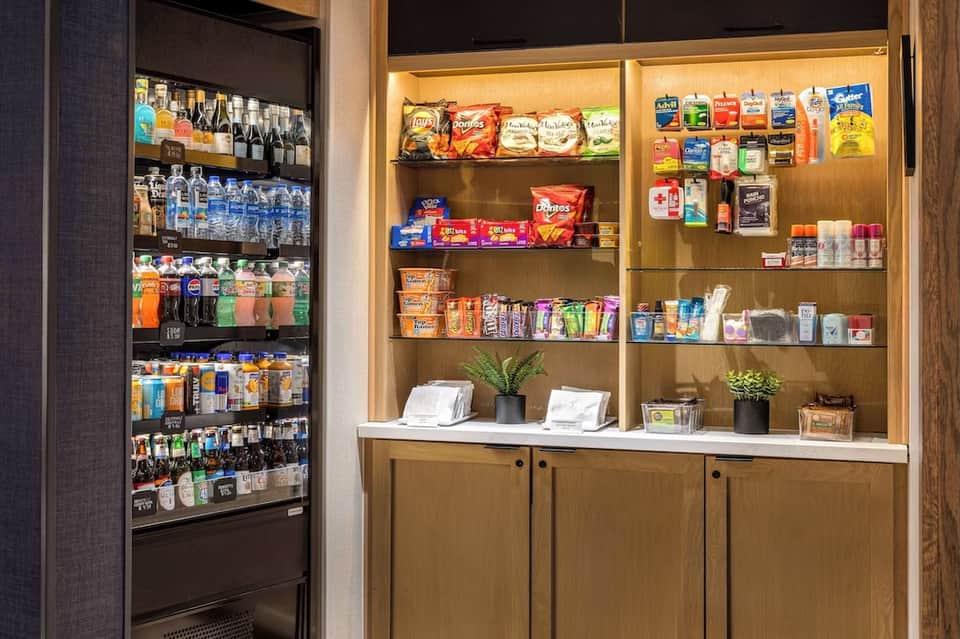 Hotel convenience store with refrigerated beverage cooler and wooden shelving stocked with snacks and amenities