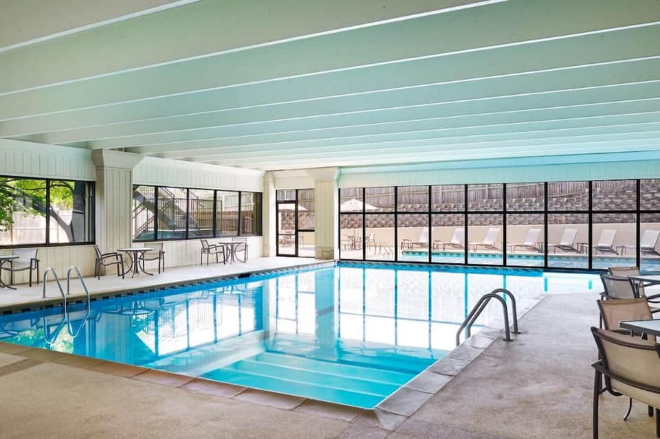Indoor heated swimming pool with large windows overlooking outdoor pool deck