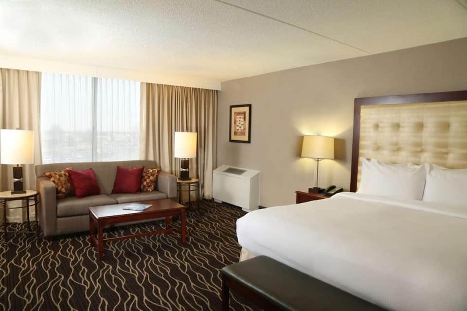 Spacious suite with king bed, sofa, panoramic windows, and modern furnishings with warm lighting