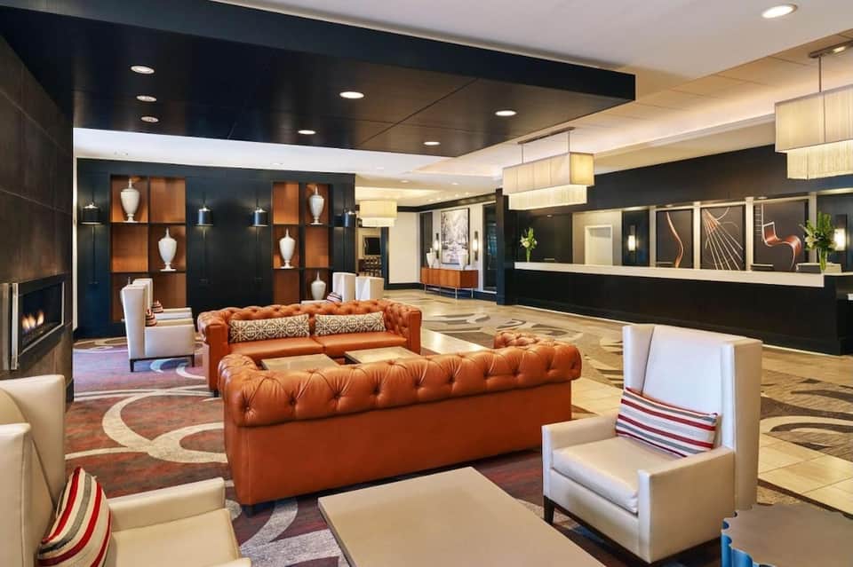 Luxury hotel lobby with orange tufted sofa, fireplace, geometric art, and modern reception desk