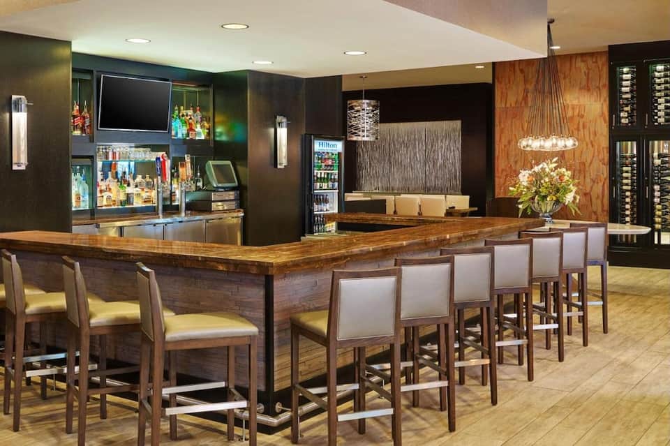 Upscale hotel bar with wooden counter, bar seating, liquor display, and pendant lighting
