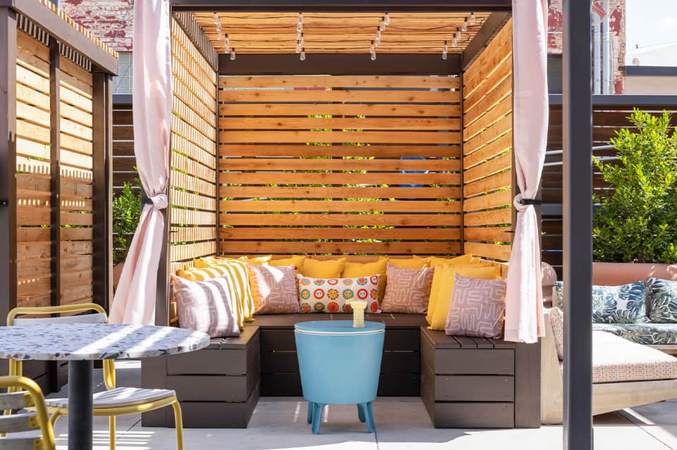 Upholstered cabana bed with pink curtains, yellow cushions, and wooden slats