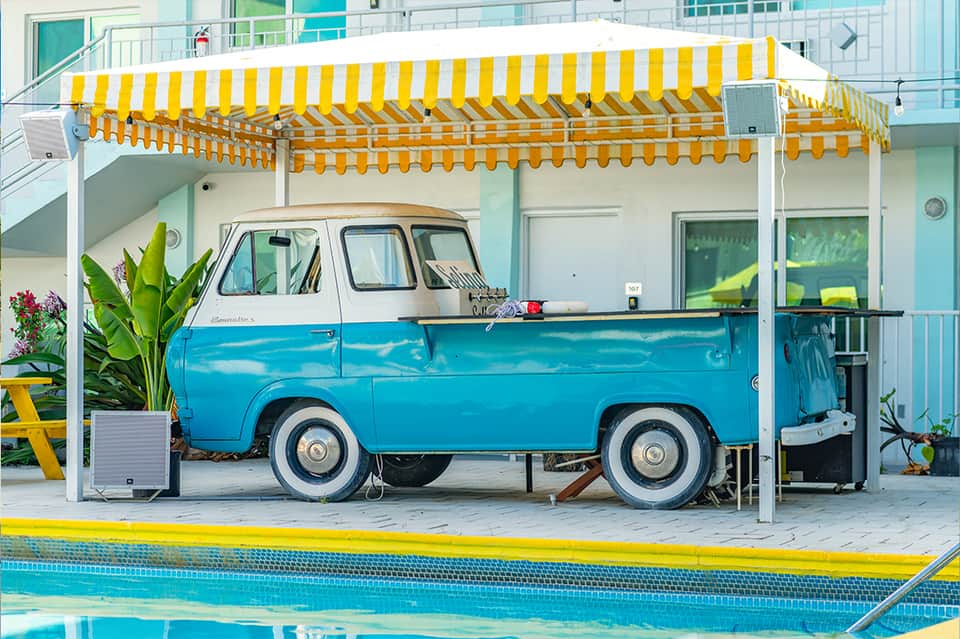 Vintage blue and white food truck under yellow striped awning by resort pool