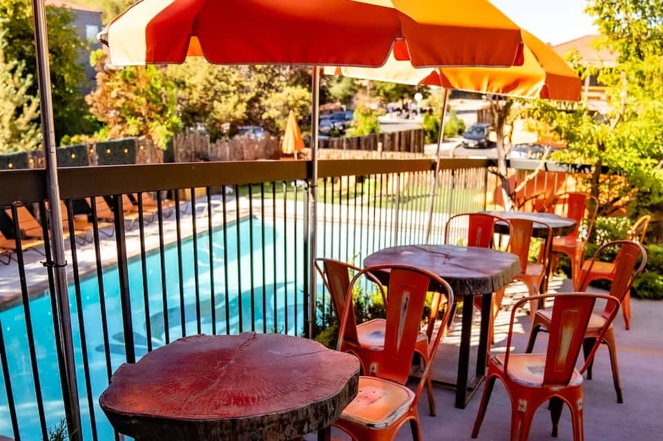 Poolside patio with red umbrellas, tables, and lush greenery
