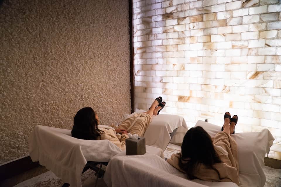 Two guests relaxing on spa loungers in salt therapy room with illuminated brick walls
