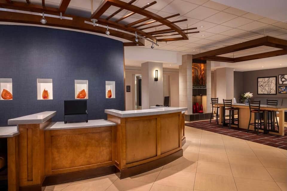 Hotel lobby with curved wooden reception desk, illuminated wall art, bar seating, and decorative elements