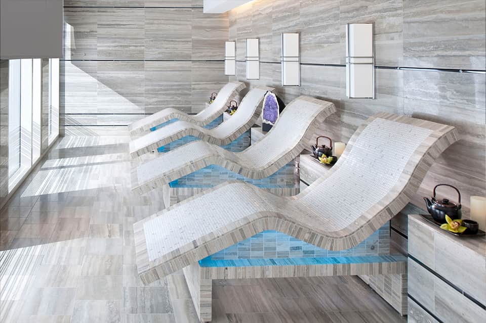 Indoor spa facility with curved loungers around heated pools in neutral tones and natural light