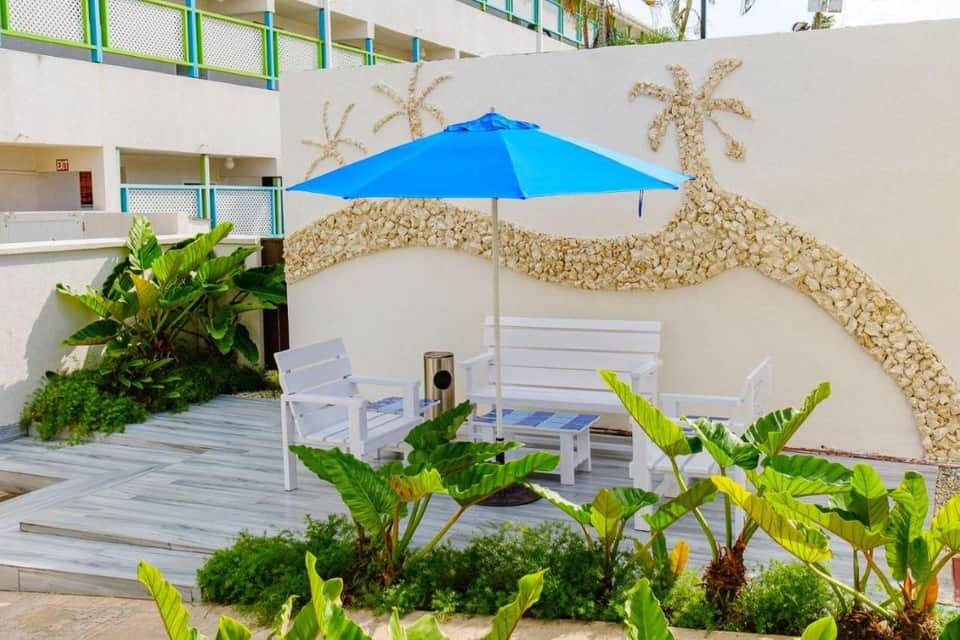 Beach-themed courtyard with seashell wall art, blue umbrella, white bench, and tropical plants