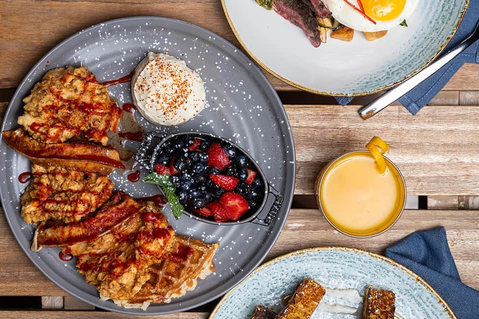 Gourmet breakfast spread with waffles, eggs, bacon, fresh berries, and orange juice on wooden table