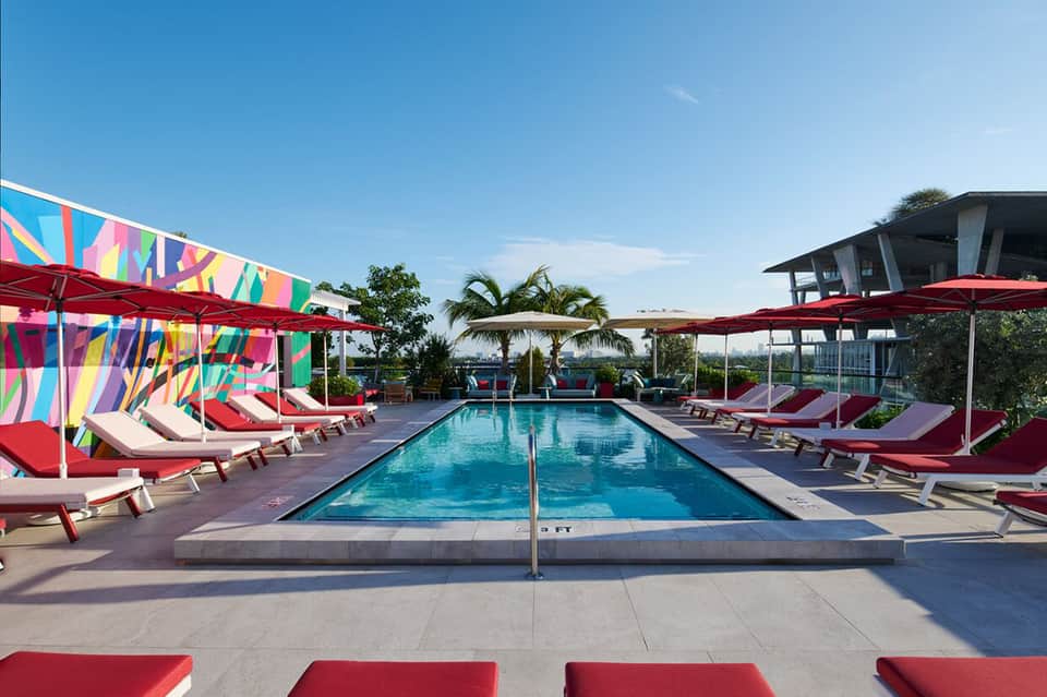 Resort pool with colorful umbrellas, red lounge chairs, and palm trees