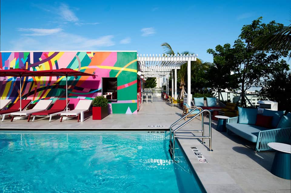 Rooftop pool area with colorful mural, lounge chairs, and pergola structure
