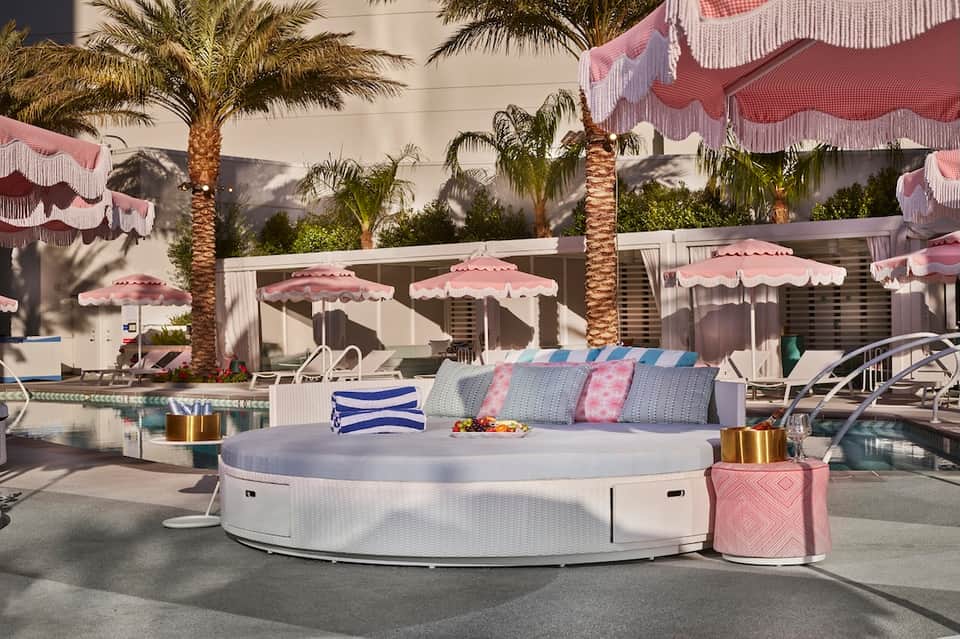 Luxurious pool deck with white circular seating, pink umbrellas, palm trees, and lounge chairs