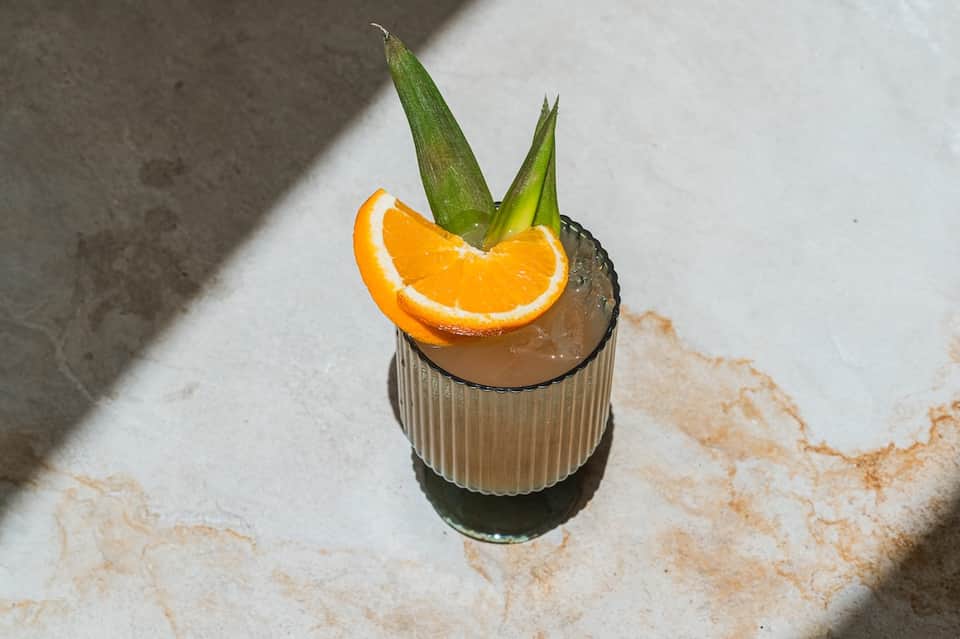 Tropical cocktail with orange slice and green leaves on concrete resort deck in sunlight