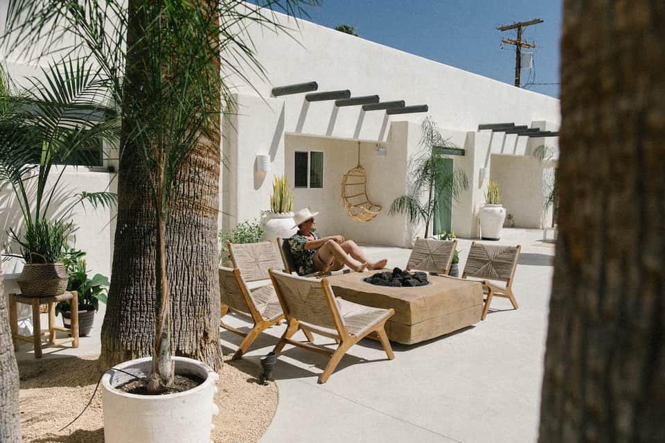 Minimalist courtyard lounge with wooden chairs, fire pit, palms, and white pergola shade
