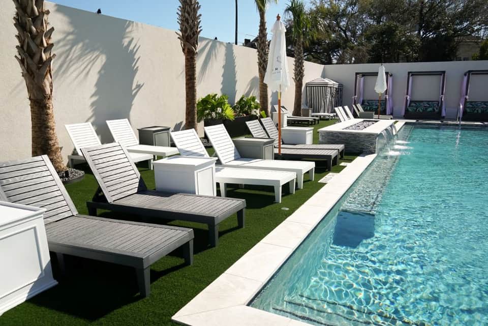Resort pool area with white lounge chairs, palm trees, umbrellas, and manicured lawn