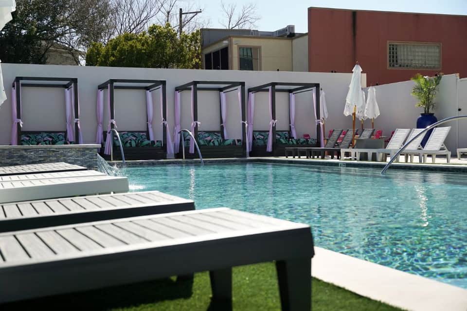 Modern pool with purple canopy cabanas, white lounge chairs, and contemporary resort buildings