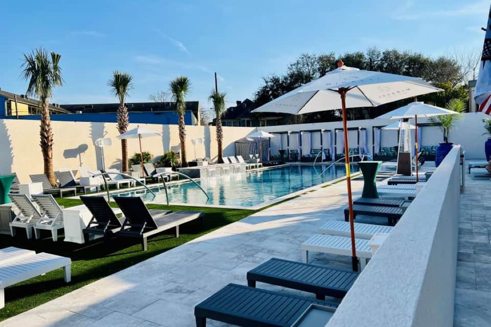 Daytime resort pool surrounded by palm trees, white umbrellas, and lounge seating