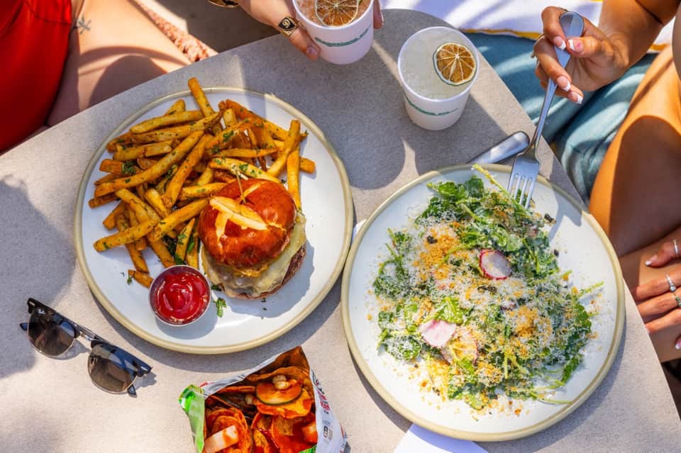 Poolside dining spread with burger, salad, fries, and lemon water beverages
