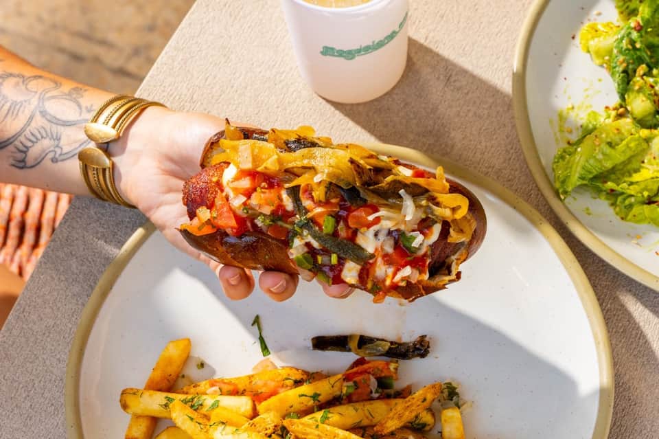 Gourmet hot dog with toppings and crispy fries served on white plate at restaurant