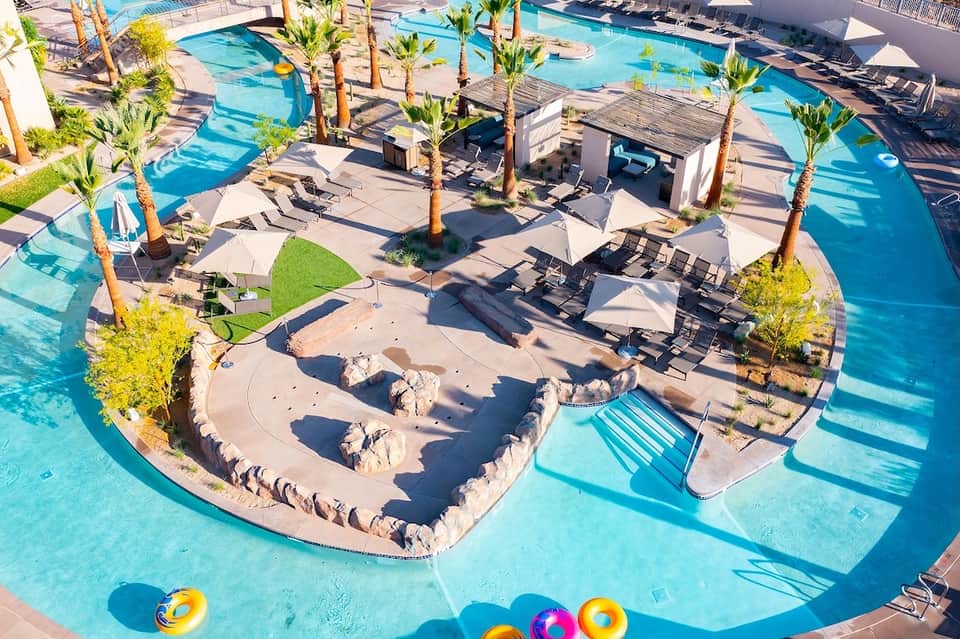 Aerial view of resort pool complex with palm trees, loungers, and sandy beach areas