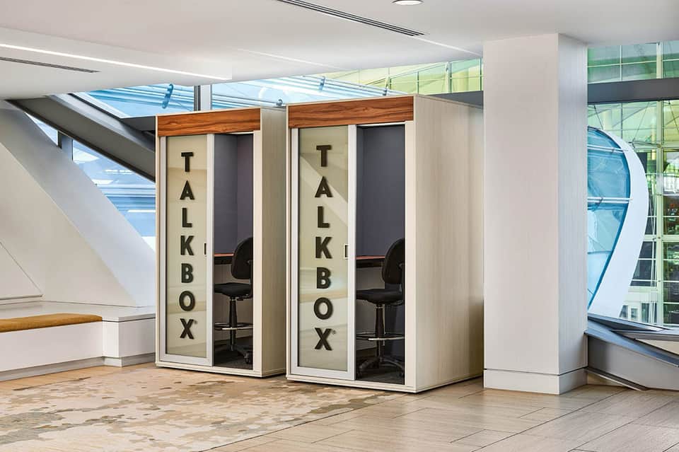 Two talk box phone booths with wood trim and glass panels in modern hotel hallway