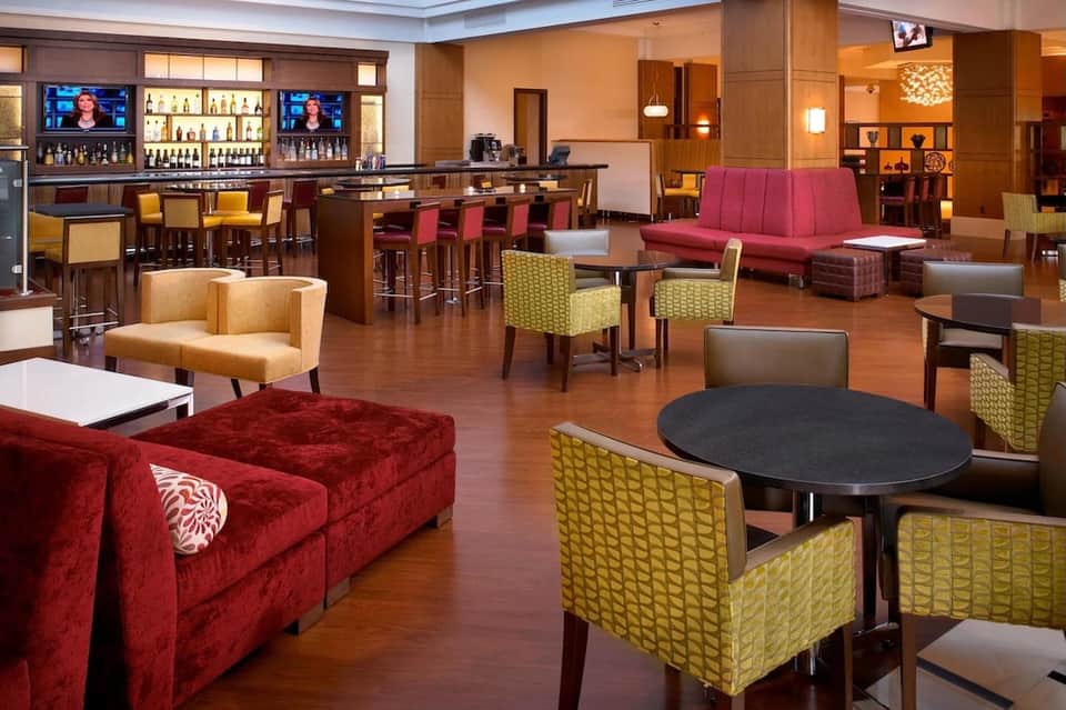 Elegant lounge area with red velvet seating, mustard chairs, wood bar, and ambient lighting