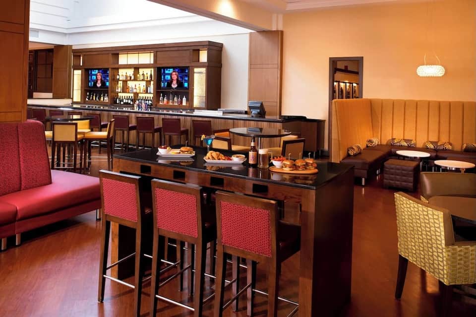 Hotel bar and lounge with dark wood accents, red seating, and ambient pendant lighting