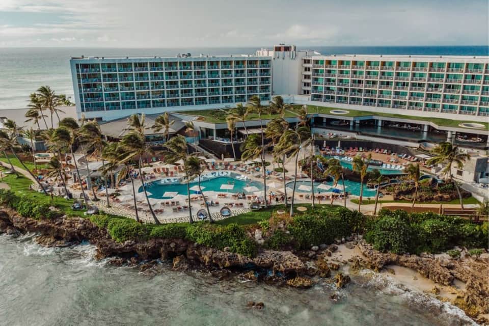 Beachfront resort with blue and green balconies, multiple pools, and tropical vegetation