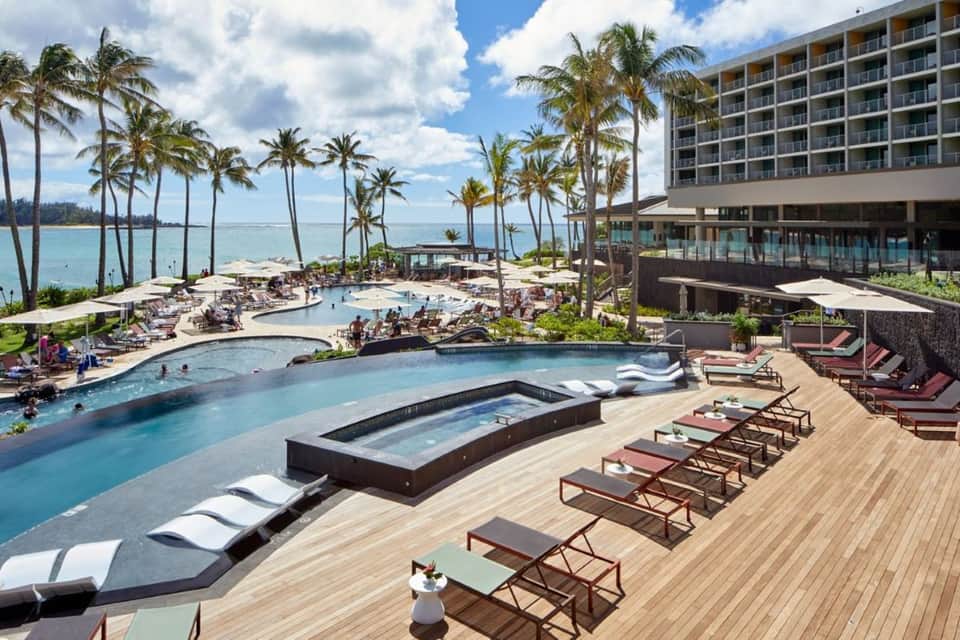 Beachfront resort pool complex with palm trees, ocean view, spa, and high-rise building