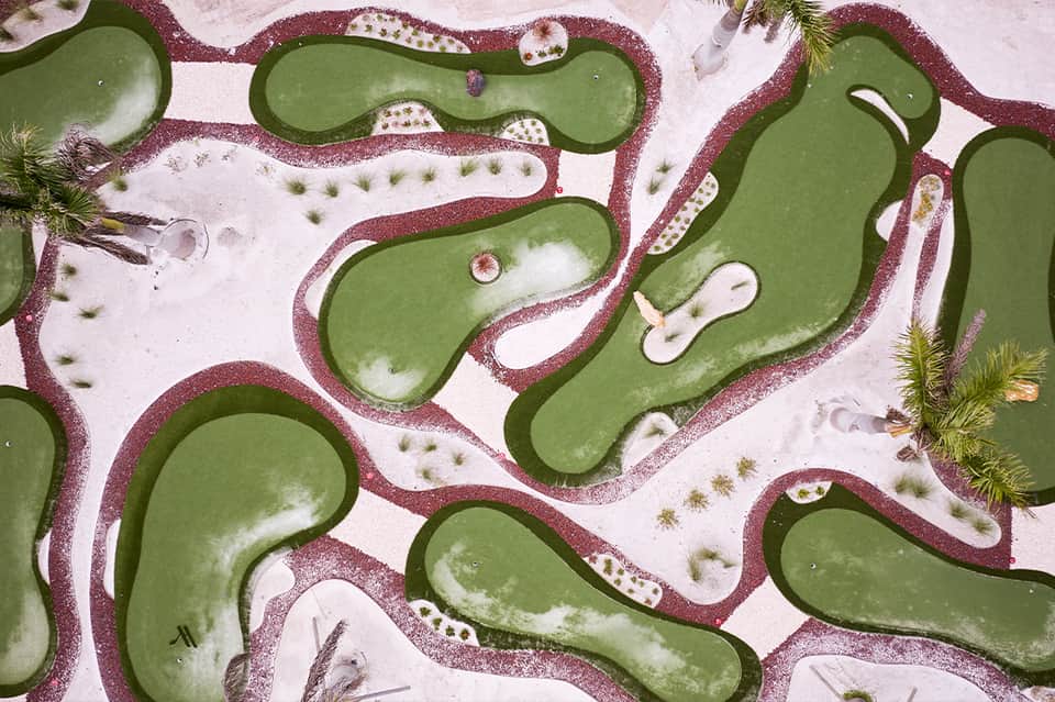 Aerial view of miniature golf course with curved green fairways bordered by burgundy sand